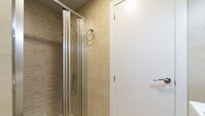 Une douche avec une porte en verre et un porte-serviettes, située à côté d’une porte blanche avec une poignée argentée.