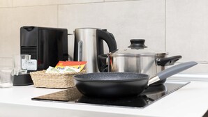 Un plan de travail de cuisine avec une poêle, une bouilloire, une casserole, une machine à café, un verre et un panier contenant des en-cas.