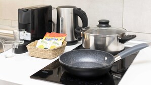 Une cuisine équipée d’une machine à café, d’une bouilloire, d’une poêle, d’une casserole, d’un verre et d’un panier contenant des sachets de café.