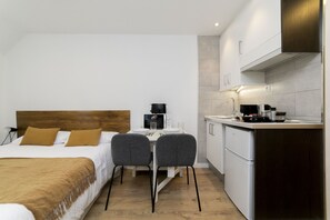 A compact hotel room with a bed, a small dining table with two chairs, a kitchenette, and a wooden headboard. - Luxury VI - Ferga Suites (Madrid)