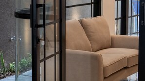 A modern interior with a glass door leading to a balcony, a beige sofa, and a view of the outside.
