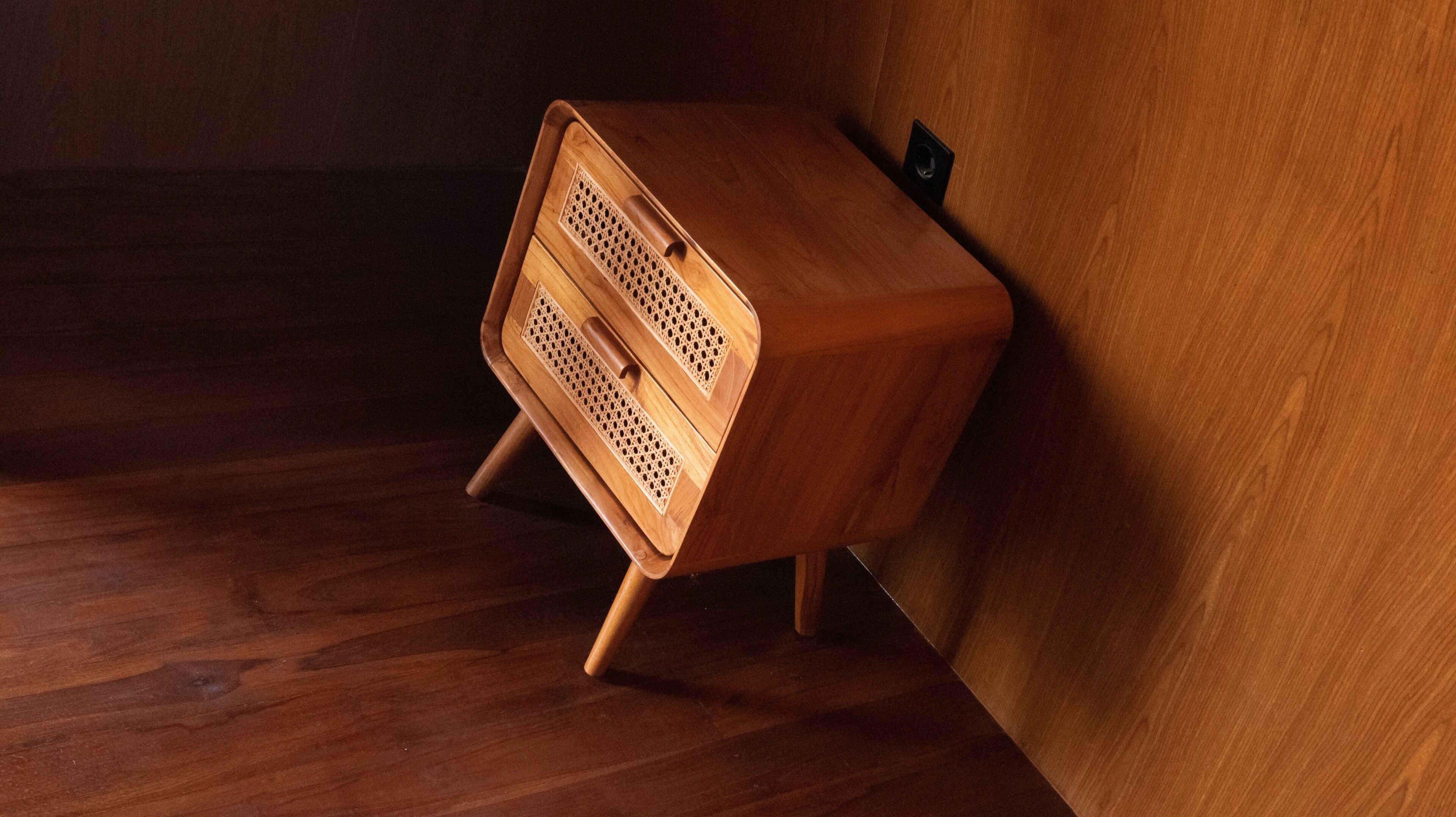 Un mueble de madera con un tirador y un pequeño estante, colocado contra una pared de madera.