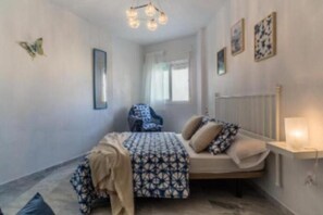 A bedroom with a bed, a chair, a bedside table with a lamp, and a window. - Villa Gaviota: Beachfront Luxury in Marina del Este - Book Now! (Almuñécar)