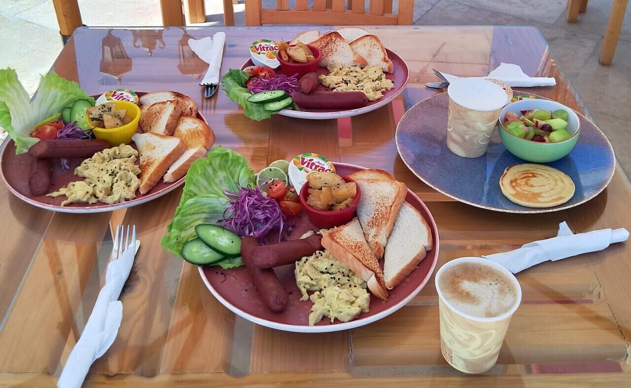Una mesa dispuesta con platos de comida, incluyendo salchichas, huevos revueltos y tostadas, junto con tazas de café y una ensalada.