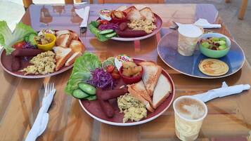 Una mesa dispuesta con platos de comida, incluyendo salchichas, huevos revueltos y tostadas, junto con tazas de café y una ensalada.