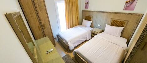 Habitación de hotel con dos camas, una mesita de noche con un control remoto, un espejo y una ventana con cortinas.