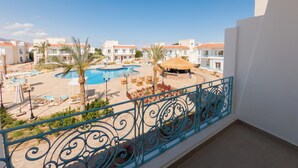 A pool area with lounge chairs, a thatched-roof structure, and a view of white buildings with orange roofs. - Blue Residence Dahab (Dahab)