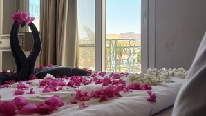 A hotel room with a bed adorned with pink and white flower petals, a decorative mirror, and a view of a balcony with a railing. - Blue Residence Dahab (Dahab)