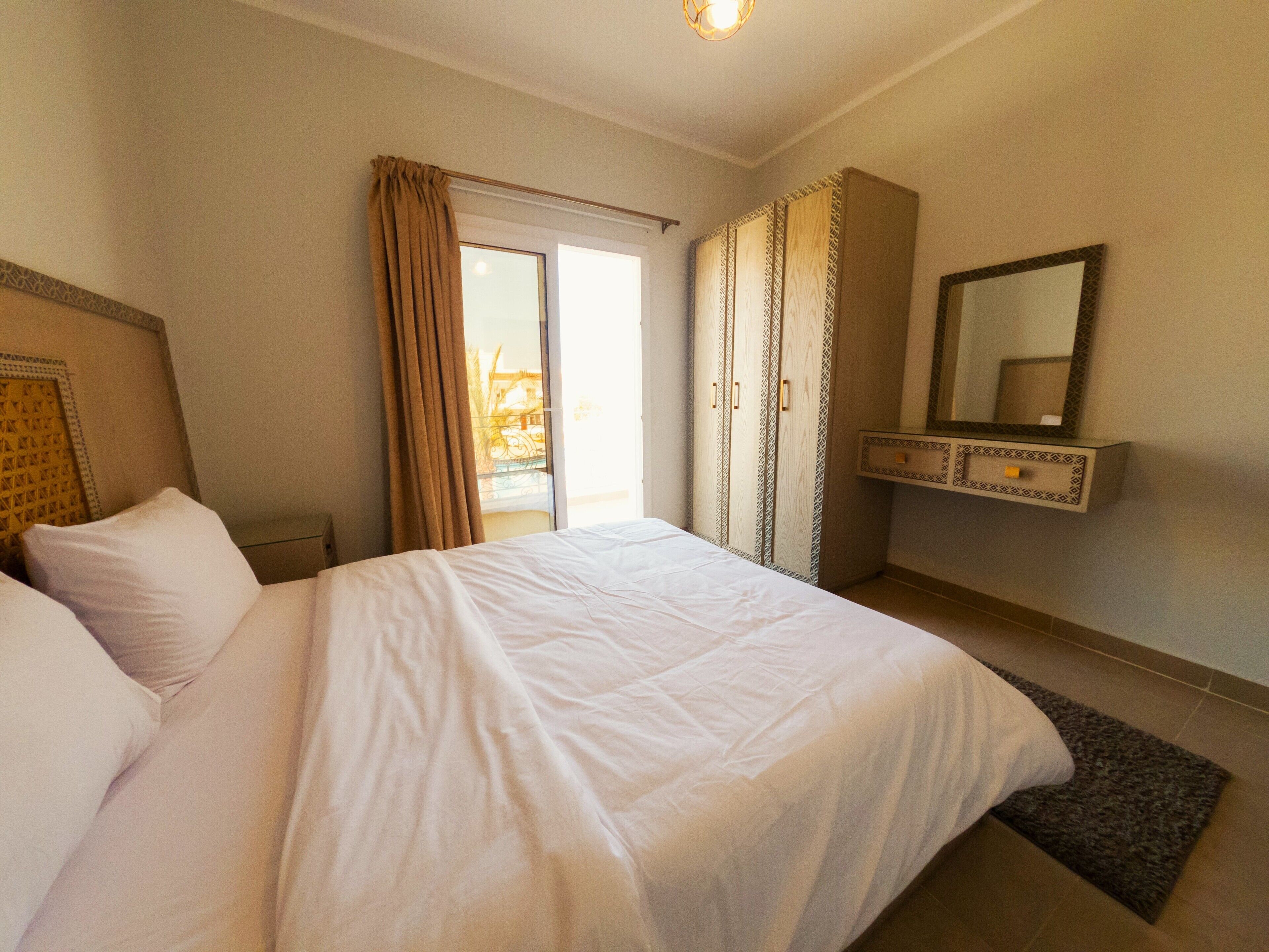 Quarto de hotel com uma cama grande, um guarda-roupa, um espelho e uma porta de correr para a varanda.