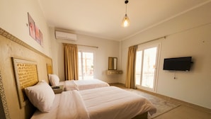 A hotel room with two beds, a flat-screen TV, a window with curtains, and an air conditioning unit. - Blue Residence Dahab (Dahab)