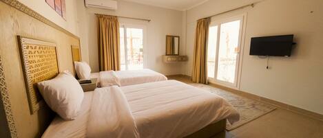 A hotel room with two beds, a flat-screen TV, a window with curtains, and an air conditioning unit.