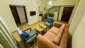 A living room with a sofa, two armchairs, a coffee table, and a TV. There is a kitchen area with cabinets and a microwave. - Blue Residence Dahab (Dahab)