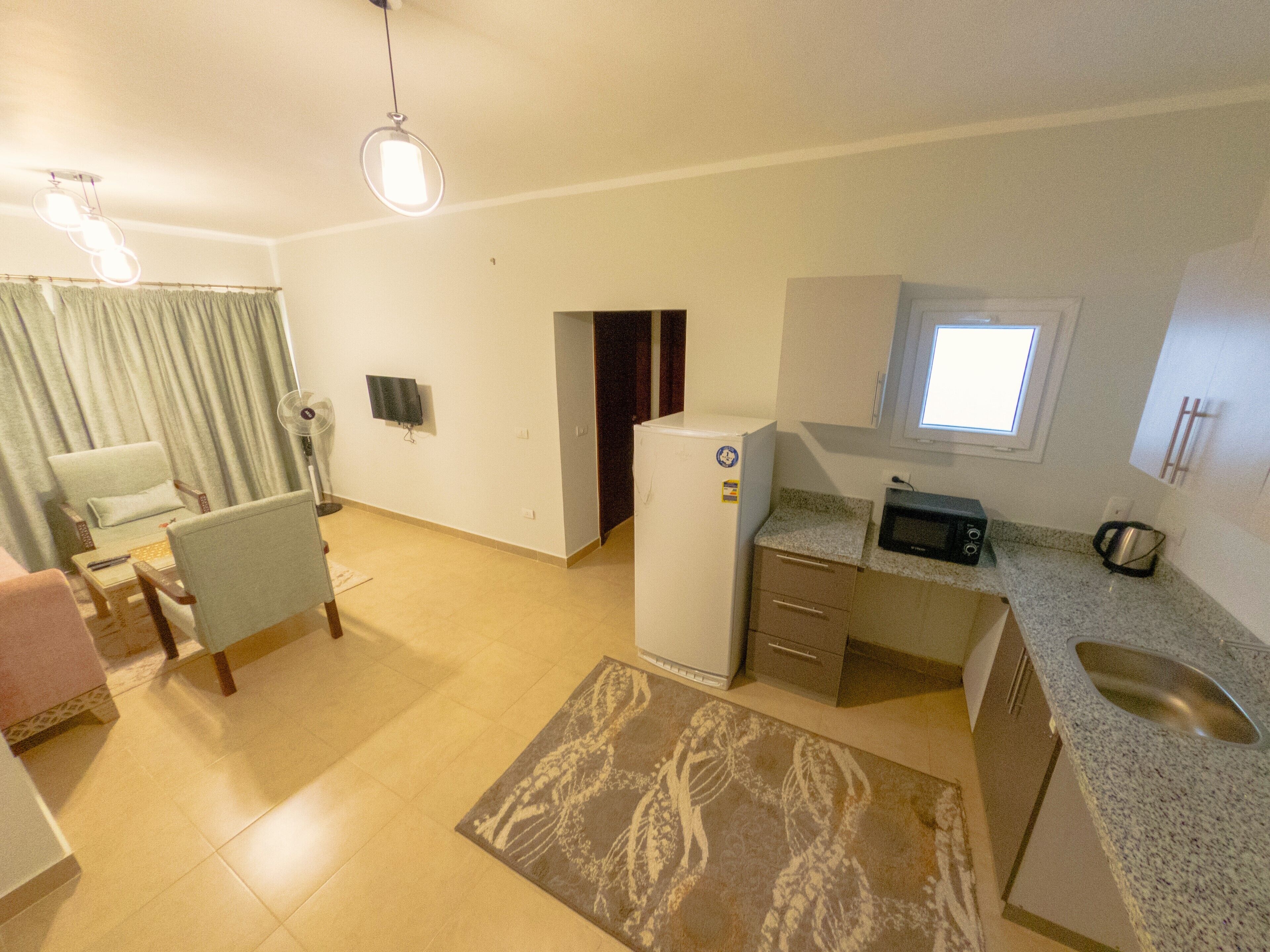 Un espacio habitable compacto con kitchenette, una zona de comedor con mesa y sillas, un sofá pequeño y un tapete estampado.