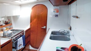 A compact kitchen with a stove, sink, and wooden door. A fire blanket is mounted on the wall. - Sleep Under the Stars on a Sailing Catamaran near Amsterdam (Monnickendam)
