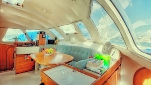 A compact boat interior with a dining area, a cushioned seating area, and a small kitchenette. - Sleep Under the Stars on a Sailing Catamaran near Amsterdam (Monnickendam)