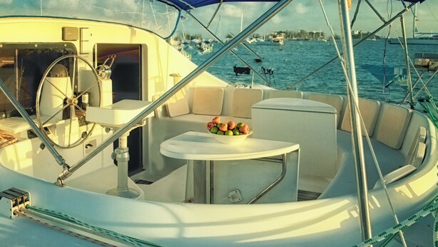 A boat interior with a dining table, cushioned seating, and a bowl of fruit. - Sleep Under the Stars on a Sailing Catamaran near Amsterdam (Monnickendam)