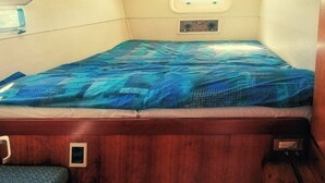 A small cabin with a single bed, a small window, and a control panel. - Sleep Under the Stars on a Sailing Catamaran near Amsterdam (Monnickendam)