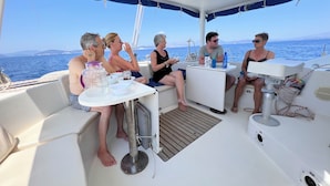 A group of people on a boat with a table and chairs, a small kitchen area, and a view of the sea. - Sleep Under the Stars on a Sailing Catamaran near Amsterdam (Monnickendam)