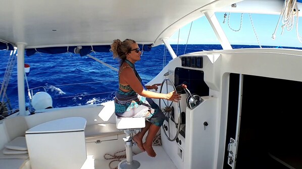 A woman steering a boat, with a white cabin and a view of the ocean. - Sleep Under the Stars on a Sailing Catamaran near Amsterdam (Monnickendam)