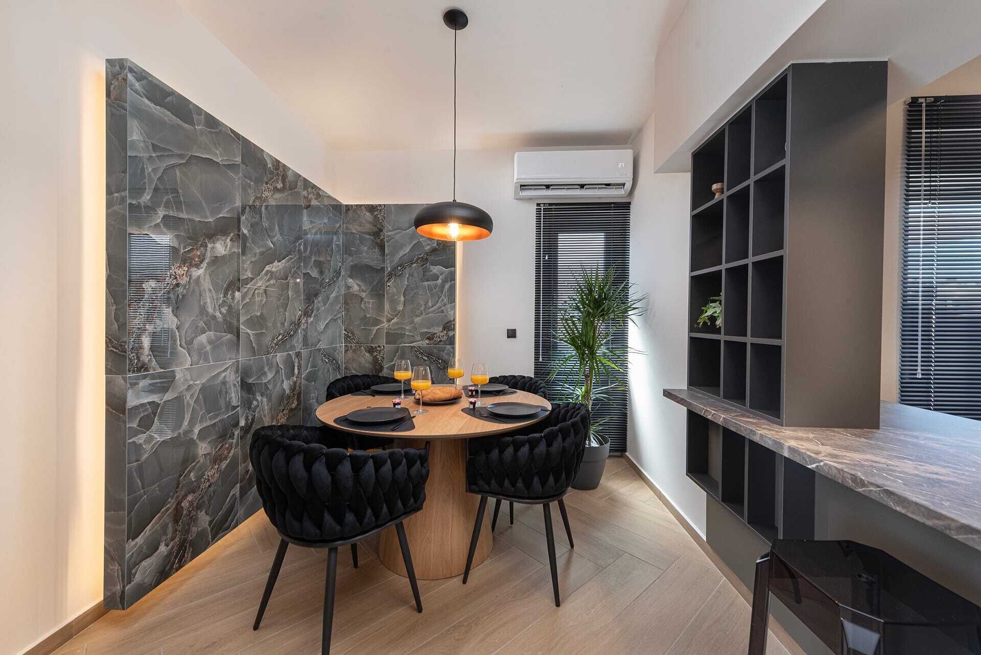 A modern dining area with a stone wall, round table, black upholstered chairs, and a pendant light.