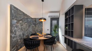 Un área de comedor moderna con pared de piedra, mesa redonda, sillas tapizadas en negro y una lámpara colgante.