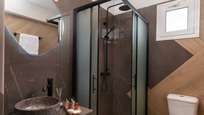 Un baño moderno con ducha de vidrio, lavamanos de mármol redondo y un inodoro blanco.