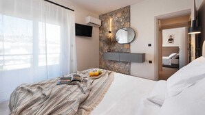 Habitación de hotel con cama, televisión montada en la pared, pared de piedra y puerta que da a otra habitación.