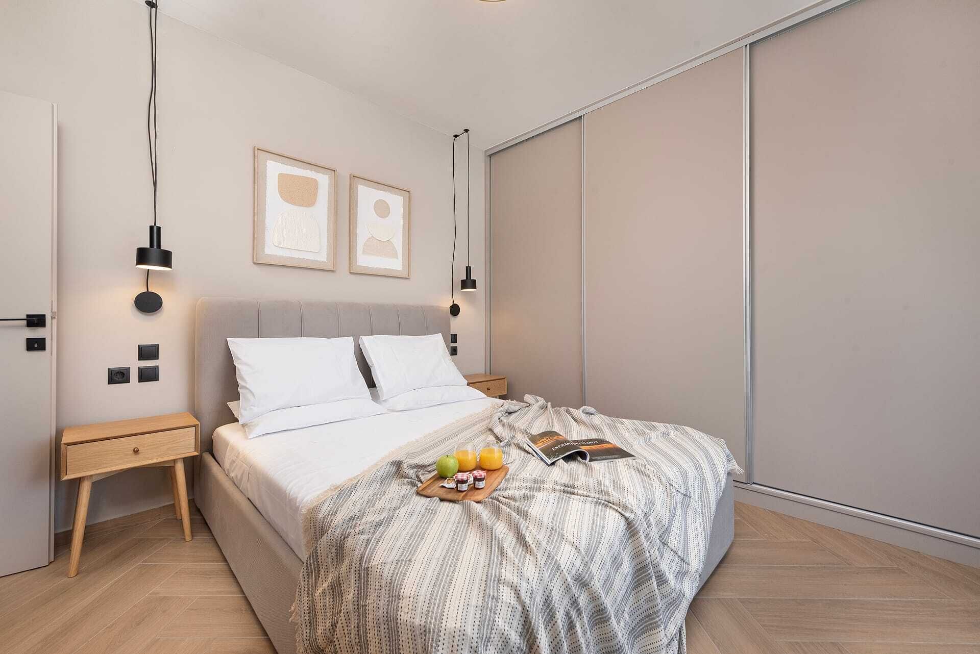 A modern bedroom with a bed, bedside tables, a wall-mounted light, and a large window.