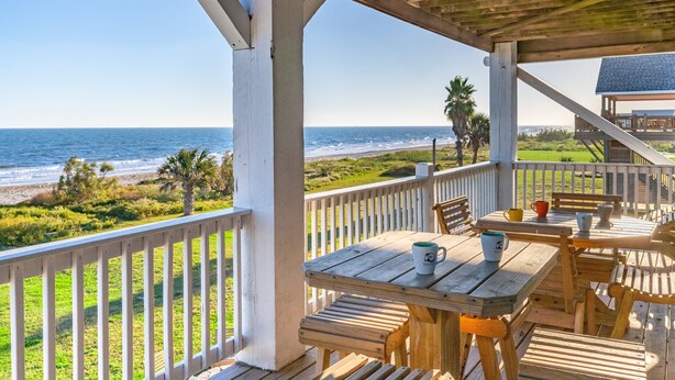 A wooden deck with tables and chairs overlooking a beach.