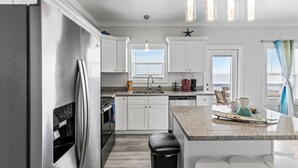 A modern kitchen with white cabinets, a stainless steel refrigerator, a granite countertop, and pendant lights.
