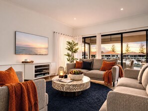 A modern living room with a sofa, armchairs, a coffee table, and a large window with a view of the sea and buildings.