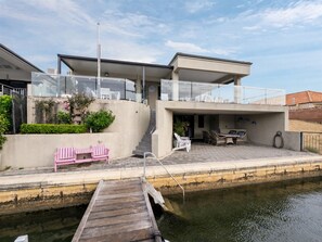 A modern house with a balcony, a wooden dock, and a patio area with outdoor furniture.