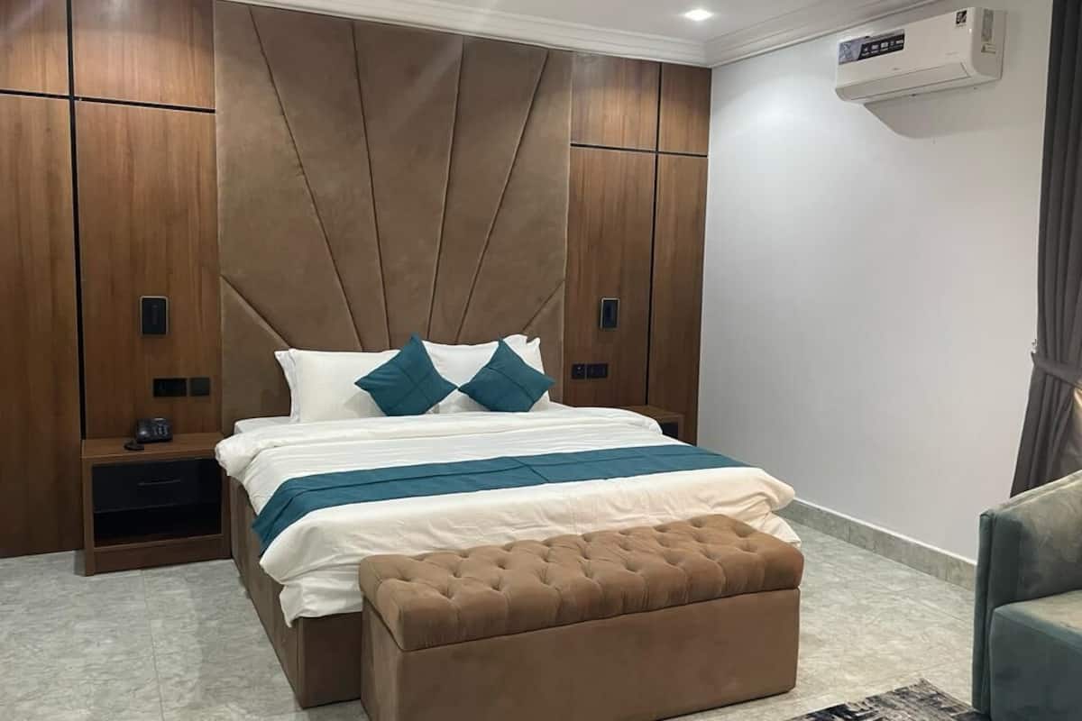 A modern bedroom with a large bed, a wooden headboard, a bedside table, and a built-in air conditioning unit.
