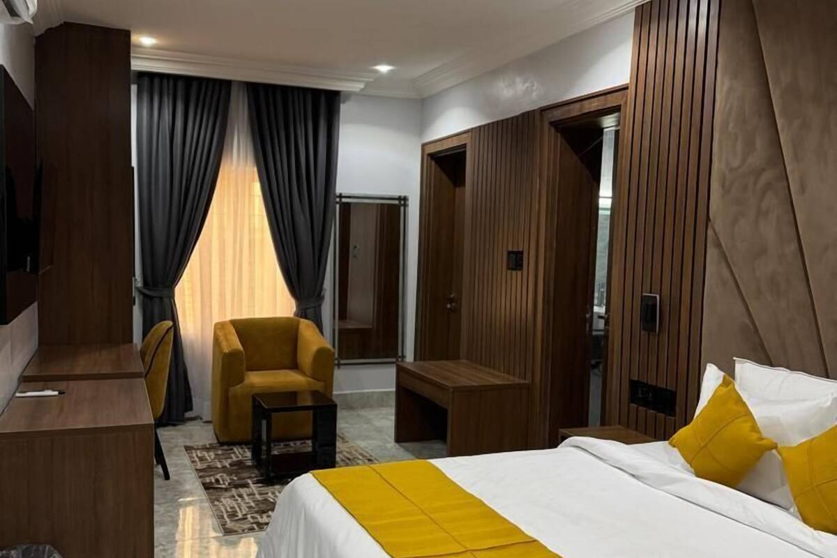 A modern hotel room with a large bed, a desk, a chair, and a sofa.