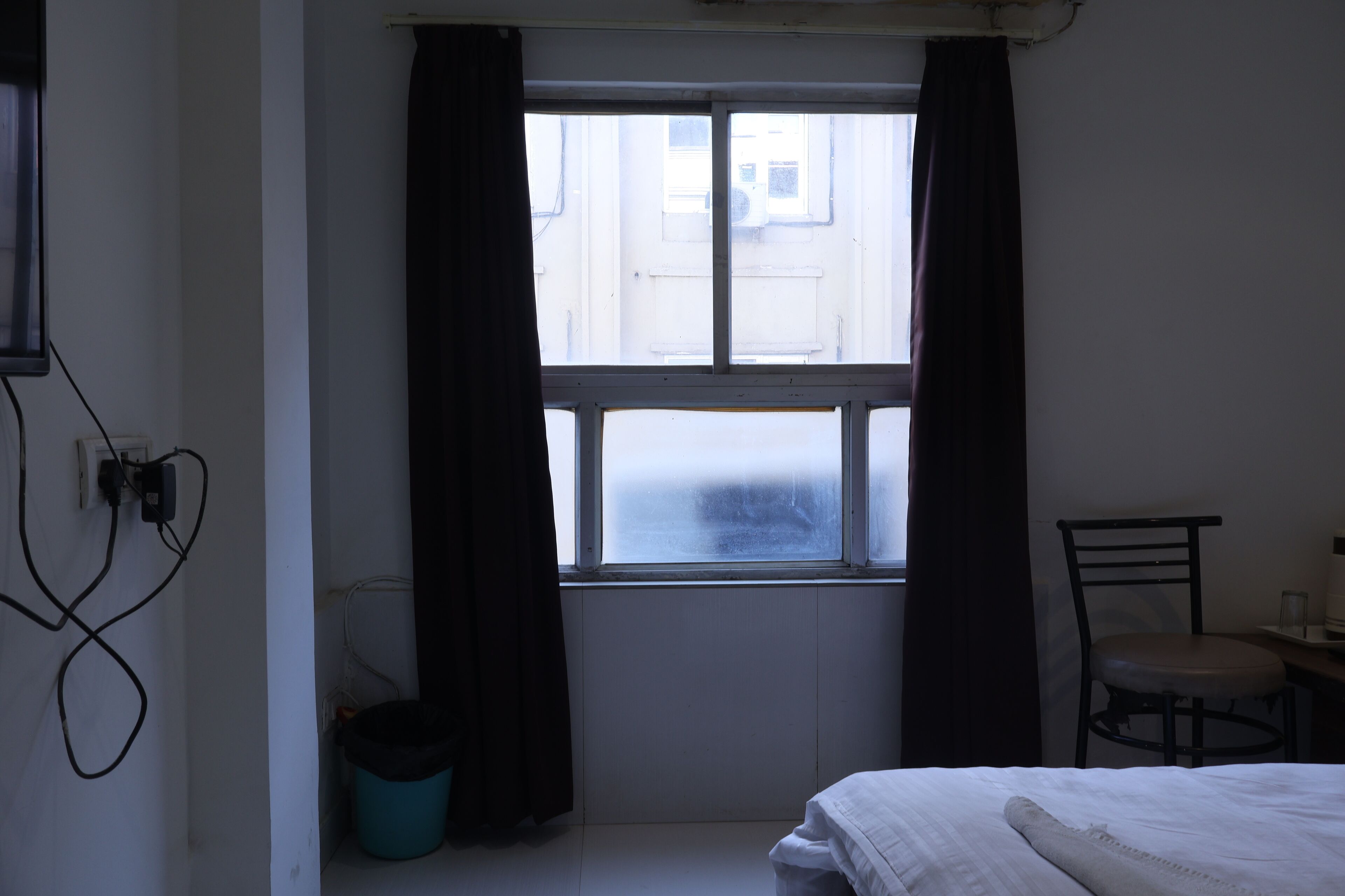 A room with a bed, a chair, a window with curtains, and a radiator.