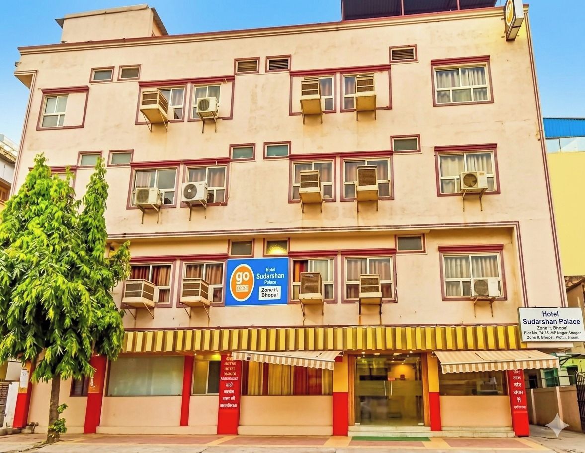 Un hôtel à plusieurs étages doté de balcons, de climatiseurs et d’une enseigne indiquant qu’il fait partie du complexe hôtelier Sudarshan Palace.