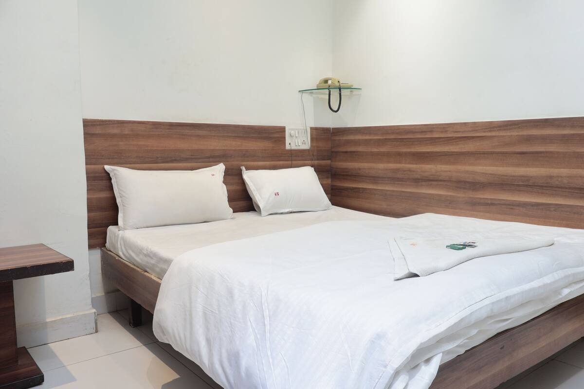 Una cama bien hecha con ropa blanca, un cabecero de madera y una mesita de noche pequeña.