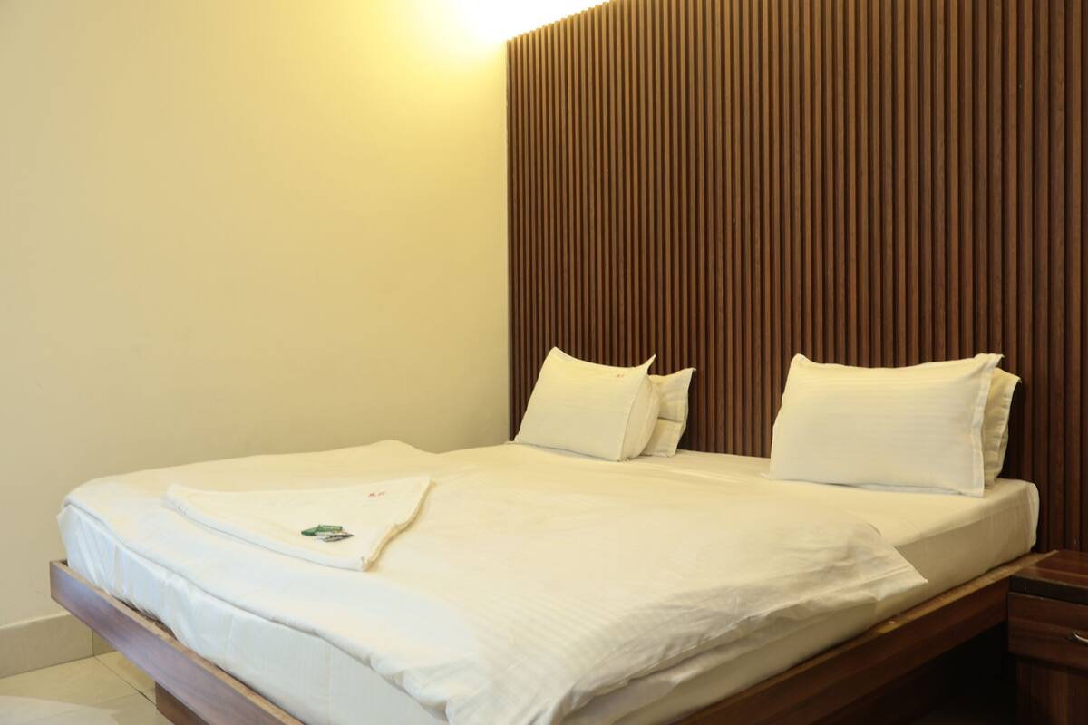 Una cama bien tendida con sábanas y almohadas blancas, un cabecero de madera y una mesita de noche con un cajón.