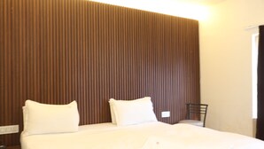 Una habitación de hotel con cama, dos almohadas, una mesita de noche y una silla.