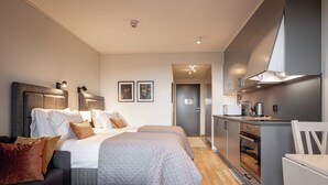 Une chambre d’hôtel moderne comprenant un lit, des tables de chevet, un canapé, un petit coin cuisine et une porte donnant sur une autre pièce.