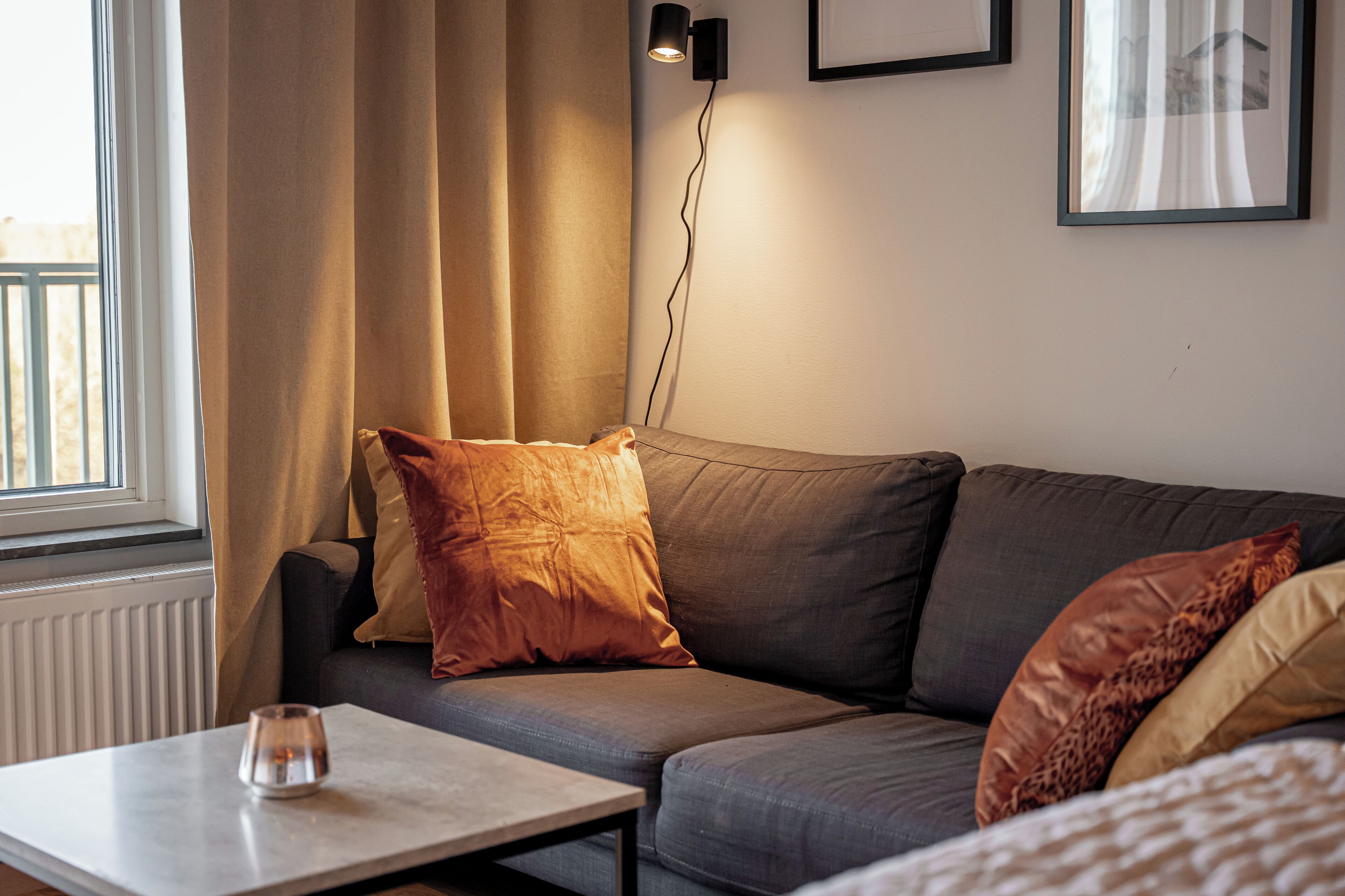 Una sala de estar moderna con sofá, una mesita de centro, una lámpara y un ventanal con cortinas.