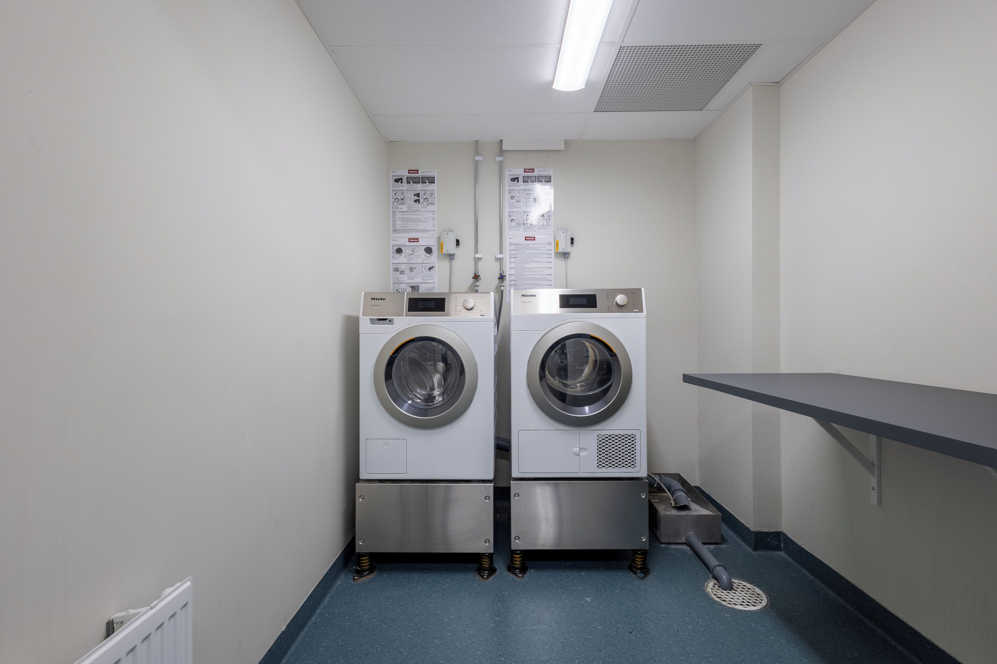 A laundry room with two front-loading washing machines, a metal sink, and a blue floor.