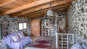 A rustic room with a wooden ceiling, stone walls, a bed with a purple blanket, a red patterned rug, and a wooden ladder. - Orgon Farm Houses (Apostoli)