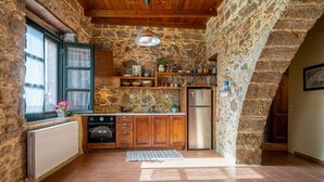 A rustic kitchen with stone walls, wooden cabinets, a stainless steel refrigerator, and a built-in oven. - Orgon Farm Houses (Apostoli)