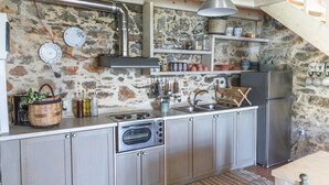 A kitchen with a stone wall, stainless steel appliances, and a wooden dining table. - Orgon Farm Houses (Apostoli)