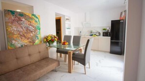 Una sala moderna con una mesa de comedor de vidrio, un sofá y una cocina con refrigerador, microondas y armarios.