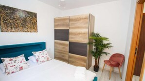 A bedroom with a bed, a wardrobe, a chair, and a plant.