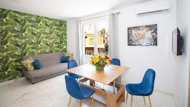 A modern living room with a grey sofa, blue chairs, a wooden dining table, and a green leafy wall. - Art Apartment IV, Two-Bedroom Apartment (Alicante (Alacant))