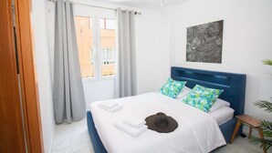 A bedroom with a bed, a ceiling fan, a window with curtains, a wall-mounted artwork, and a small bedside table with a plant. - Art Apartment IV, Two-Bedroom Apartment (Alicante (Alacant))