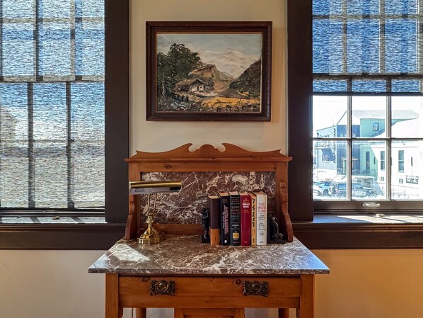 A marble-top table with books and a brass lamp, set against a window with a view of buildings.
